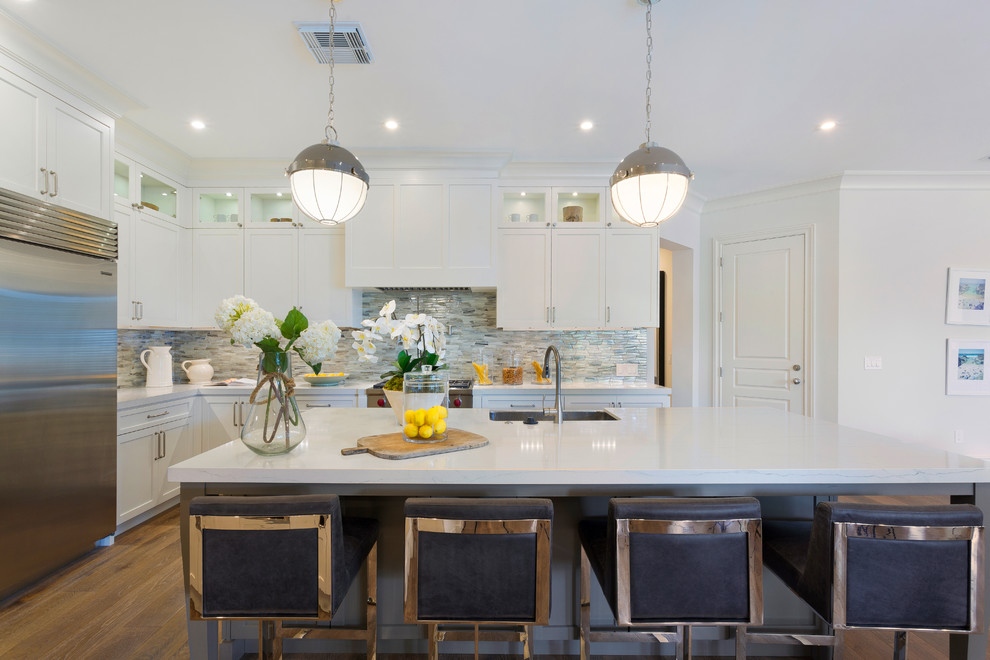 Mid-sized beach style l-shaped medium tone wood floor and brown floor kitchen photo in Other with an undermount sink, white cabinets, marble countertops, multicolored backsplash, subway tile backsplash, stainless steel appliances, an island, white countertops and shaker cabinets