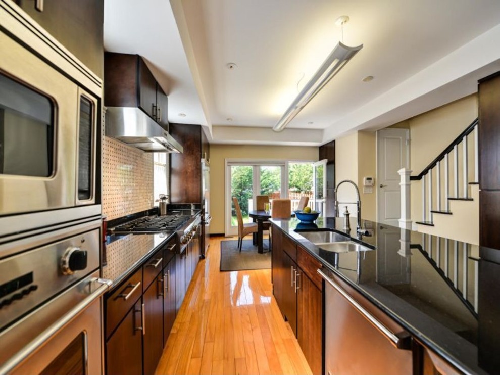This is an example of a medium sized classic galley kitchen/diner in DC Metro with a double-bowl sink, flat-panel cabinets, dark wood cabinets, engineered stone countertops, beige splashback, ceramic splashback, stainless steel appliances, medium hardwood flooring and a breakfast bar.