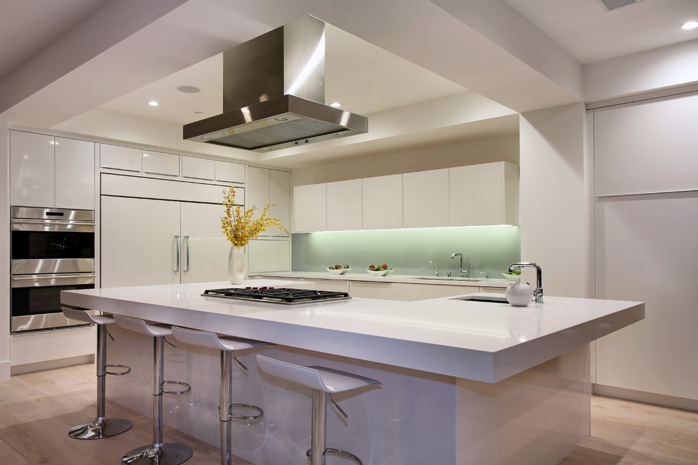Inspiration for a contemporary kitchen in Orange County with a submerged sink, flat-panel cabinets, white cabinets, glass sheet splashback, stainless steel appliances, light hardwood flooring and an island.