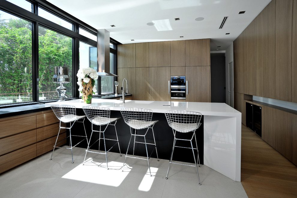 Moderne Küche in U-Form mit flächenbündigen Schrankfronten, dunklen Holzschränken, Küchengeräten aus Edelstahl, dunklem Holzboden, Halbinsel, braunem Boden und weißer Arbeitsplatte in Miami
