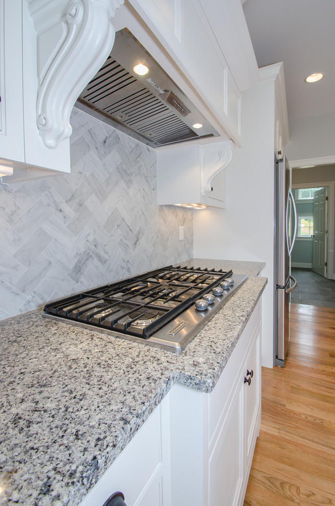 Exempel på ett mellanstort klassiskt kök, med en undermonterad diskho, luckor med profilerade fronter, vita skåp, granitbänkskiva, grått stänkskydd, stänkskydd i stenkakel, rostfria vitvaror, ljust trägolv och en köksö