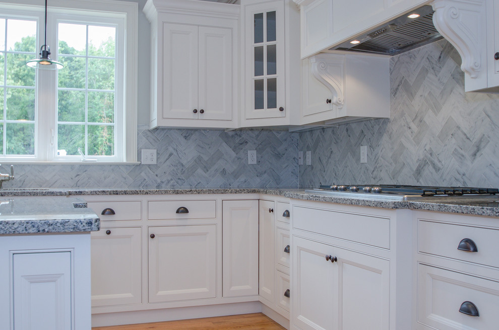 Inredning av ett klassiskt mellanstort kök, med en undermonterad diskho, luckor med profilerade fronter, vita skåp, granitbänkskiva, grått stänkskydd, stänkskydd i stenkakel, rostfria vitvaror, ljust trägolv och en köksö