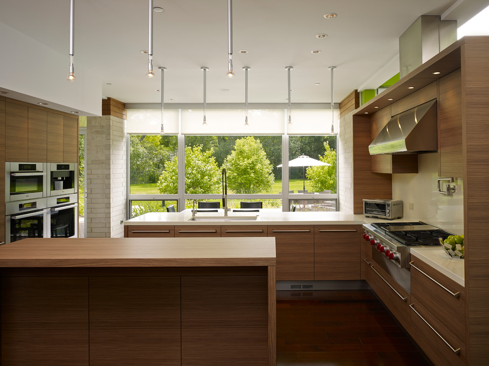 Photo of a large contemporary u-shaped kitchen/diner in Chicago with a submerged sink, medium wood cabinets, beige splashback, stainless steel appliances, an island, flat-panel cabinets, vinyl flooring and brown floors.