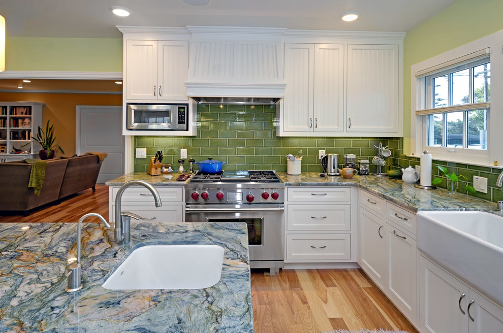 Foto på ett stort maritimt kök och matrum, med en rustik diskho, luckor med profilerade fronter, vita skåp, granitbänkskiva, grönt stänkskydd, stänkskydd i keramik, rostfria vitvaror, ljust trägolv och en köksö