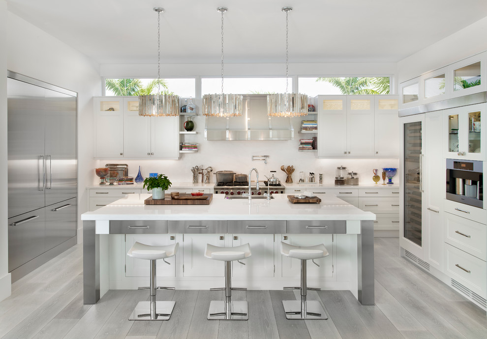Foto på ett avskilt funkis u-kök, med en köksö, skåp i shakerstil, vita skåp, vitt stänkskydd, ljust trägolv, rostfria vitvaror och grått golv