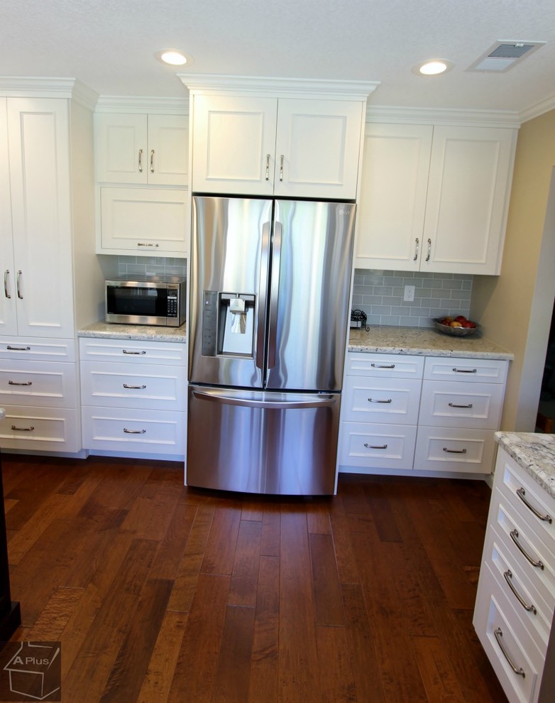 Klassisk inredning av ett mellanstort kök, med en nedsänkt diskho, luckor med infälld panel, vita skåp, granitbänkskiva, blått stänkskydd, stänkskydd i tunnelbanekakel, rostfria vitvaror, mellanmörkt trägolv och en halv köksö