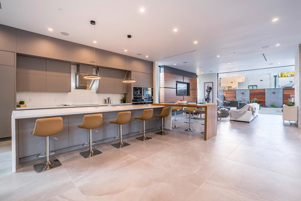 This is an example of an expansive contemporary l-shaped open plan kitchen in Los Angeles with a submerged sink, flat-panel cabinets, grey cabinets, composite countertops, white splashback, ceramic splashback, stainless steel appliances, concrete flooring, multiple islands and beige floors.