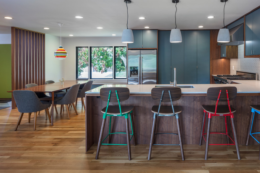 Mid-sized mid-century modern light wood floor eat-in kitchen photo in Kansas City with an undermount sink, flat-panel cabinets, blue cabinets, quartz countertops, white backsplash, ceramic backsplash, stainless steel appliances and a peninsula