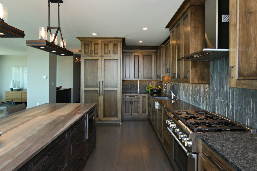 Example of a large urban l-shaped dark wood floor eat-in kitchen design in Minneapolis with a farmhouse sink, recessed-panel cabinets, dark wood cabinets, granite countertops, black backsplash, stone tile backsplash, stainless steel appliances and an island