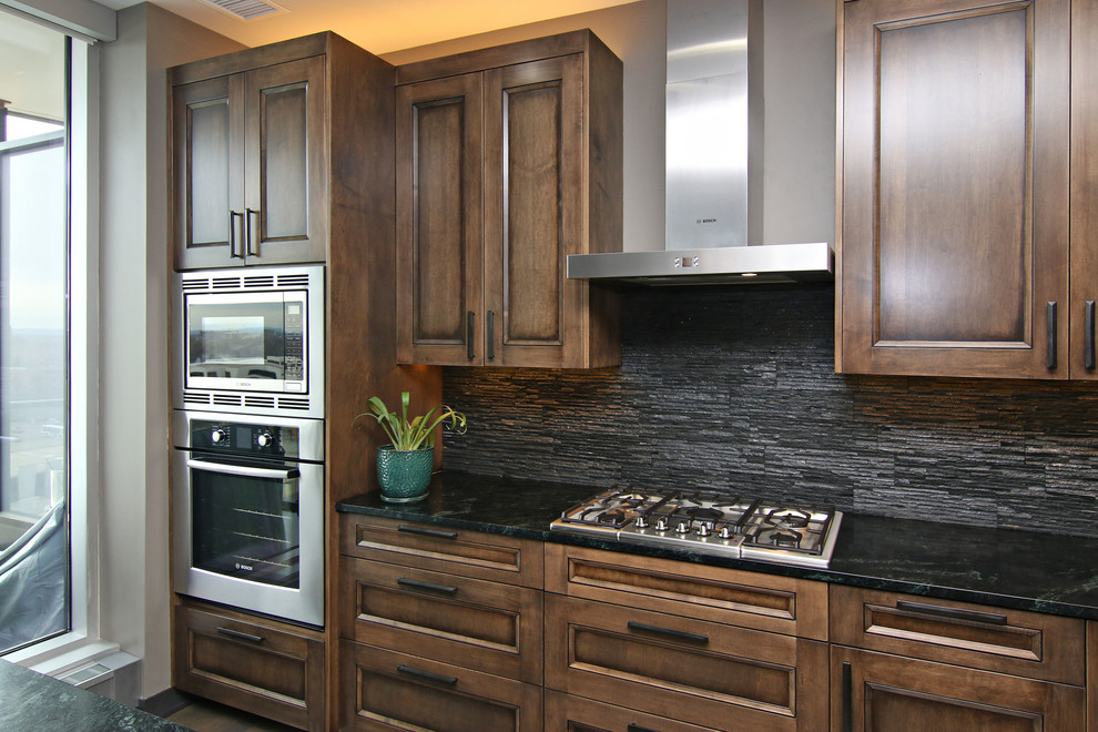 Foto på ett mellanstort funkis kök, med släta luckor, skåp i mellenmörkt trä, bänkskiva i täljsten, stänkskydd med metallisk yta, rostfria vitvaror och en köksö