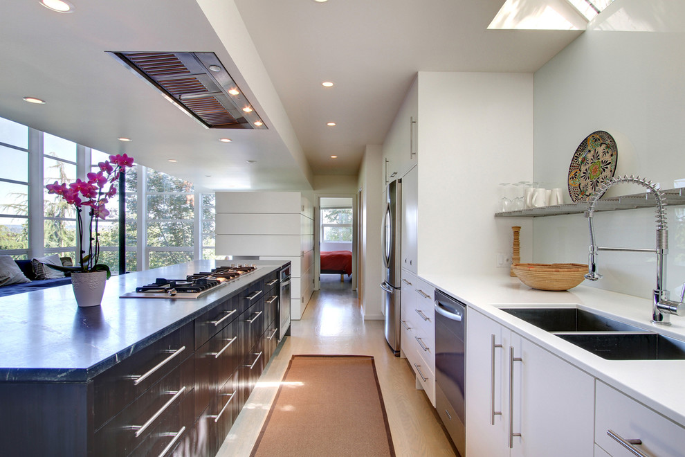 Trendy galley light wood floor open concept kitchen photo in Seattle with a double-bowl sink, flat-panel cabinets, white cabinets, glass sheet backsplash, stainless steel appliances and an island