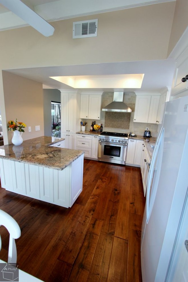 Klassisk inredning av ett stort kök, med en dubbel diskho, luckor med infälld panel, vita skåp, granitbänkskiva, beige stänkskydd, stänkskydd i stenkakel, rostfria vitvaror, mellanmörkt trägolv och en halv köksö