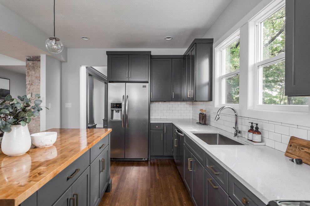 Mid-sized minimalist l-shaped medium tone wood floor and brown floor eat-in kitchen photo in Indianapolis with an undermount sink, recessed-panel cabinets, gray cabinets, wood countertops, white backsplash, subway tile backsplash, stainless steel appliances and an island