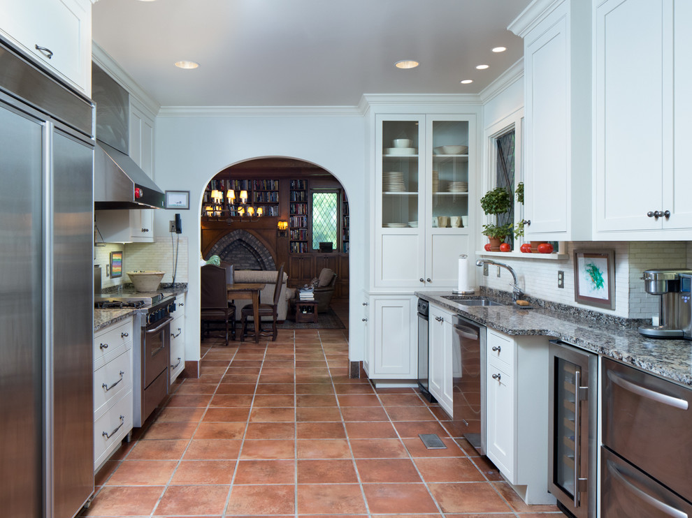Example of a large classic galley terra-cotta tile enclosed kitchen design in Birmingham with an undermount sink, flat-panel cabinets, white cabinets, granite countertops, white backsplash, stone tile backsplash, stainless steel appliances and no island