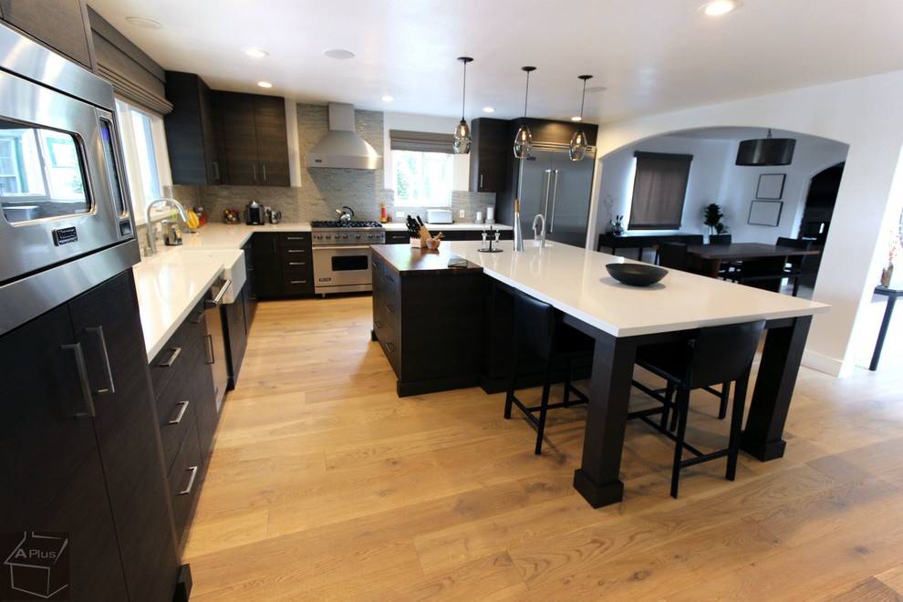Eat-in kitchen - large modern l-shaped light wood floor eat-in kitchen idea in Orange County with a farmhouse sink, flat-panel cabinets, dark wood cabinets, quartzite countertops, gray backsplash, mosaic tile backsplash, stainless steel appliances and an island