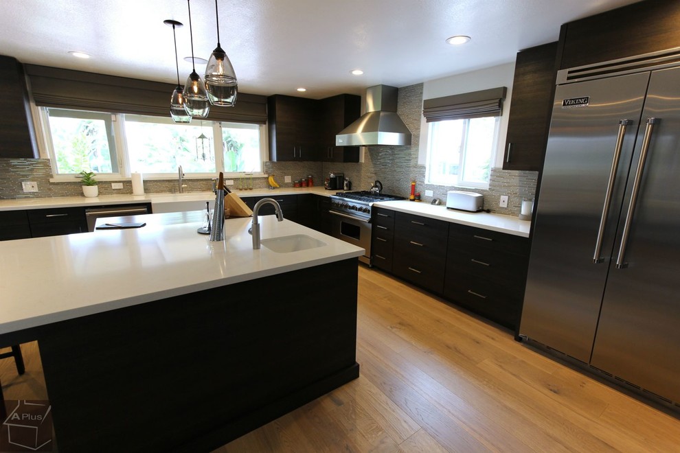 Inspiration for a large modern l-shaped light wood floor eat-in kitchen remodel in Orange County with a farmhouse sink, flat-panel cabinets, dark wood cabinets, quartzite countertops, gray backsplash, mosaic tile backsplash, stainless steel appliances and an island