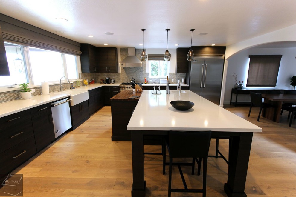 Large minimalist l-shaped light wood floor eat-in kitchen photo in Orange County with a farmhouse sink, flat-panel cabinets, dark wood cabinets, quartzite countertops, gray backsplash, mosaic tile backsplash, stainless steel appliances and an island