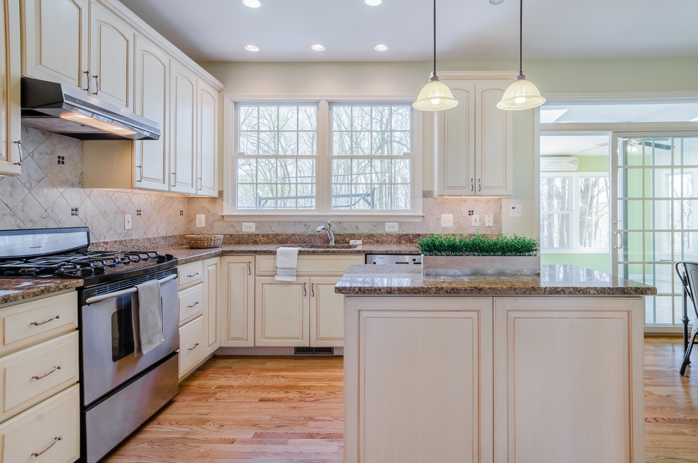 Example of a mid-sized eclectic l-shaped medium tone wood floor and brown floor open concept kitchen design in Baltimore with an undermount sink, shaker cabinets, white cabinets, granite countertops, beige backsplash, stone tile backsplash, stainless steel appliances and an island