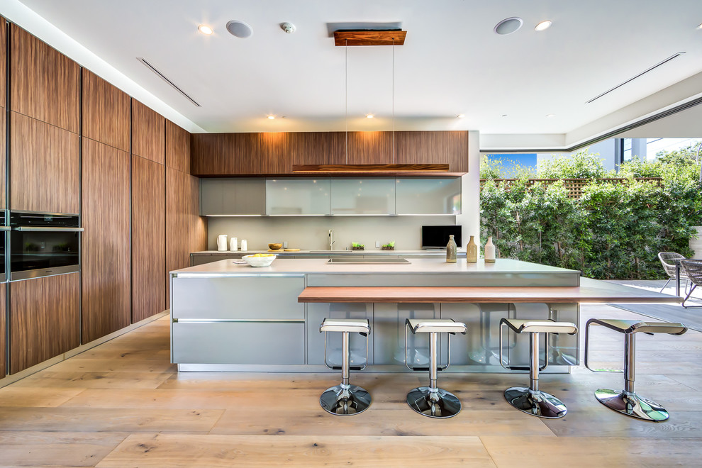 This is an example of a large contemporary single-wall open plan kitchen in Los Angeles with brown cabinets, granite worktops, grey splashback, light hardwood flooring and an island.