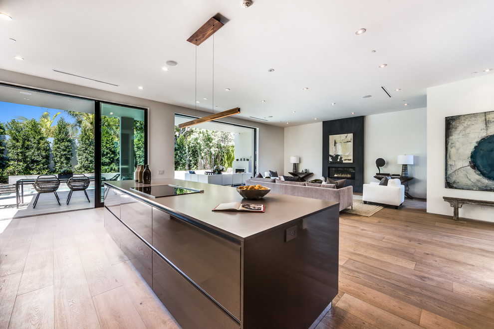 Large modern single-wall open plan kitchen in Los Angeles with brown cabinets, granite worktops, grey splashback, light hardwood flooring, an island, an integrated sink and stainless steel appliances.
