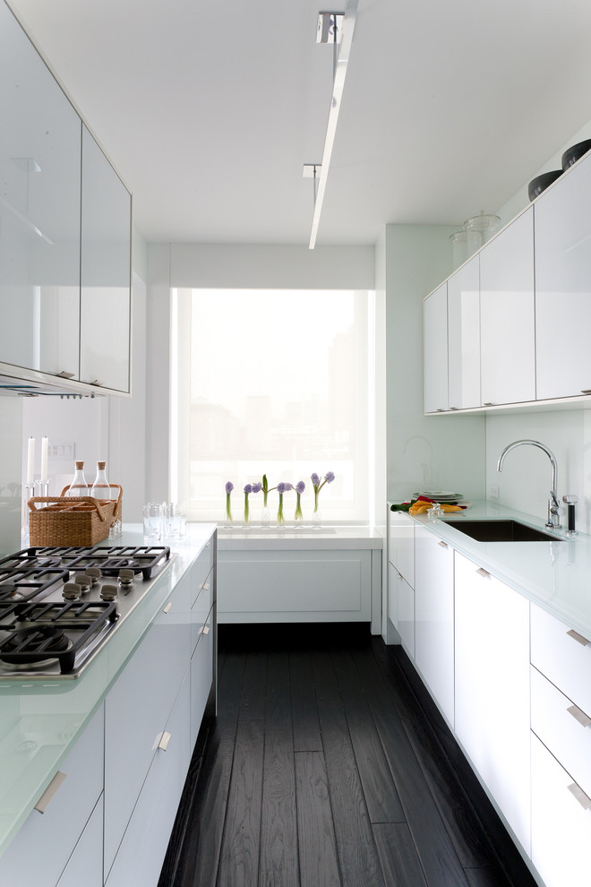 Zweizeilige, Geschlossene Moderne Küche mit Waschbecken, flächenbündigen Schrankfronten, weißen Schränken, Glas-Arbeitsplatte und Küchenrückwand in Weiß in New York