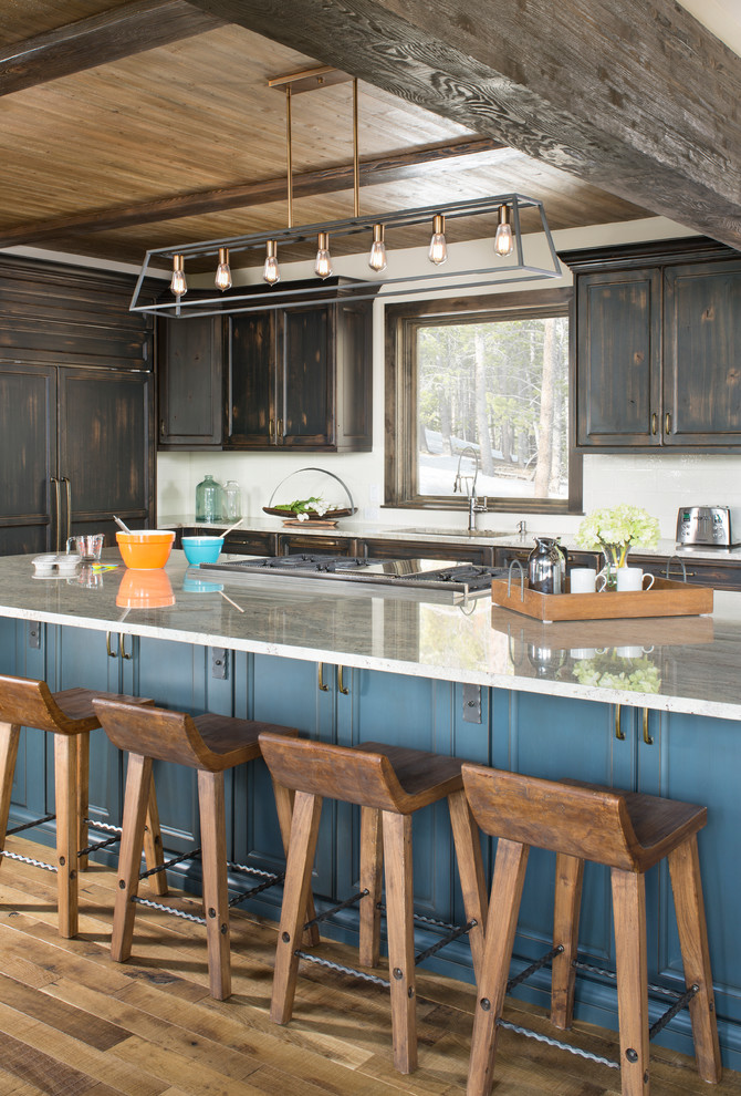 Rustik inredning av ett grå grått l-kök, med en undermonterad diskho, luckor med infälld panel, skåp i slitet trä, integrerade vitvaror, mellanmörkt trägolv, en köksö och brunt golv