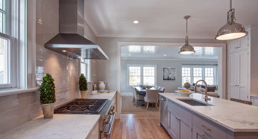 Example of a large beach style u-shaped light wood floor and brown floor eat-in kitchen design in Other with an undermount sink, recessed-panel cabinets, white cabinets, marble countertops, gray backsplash, ceramic backsplash, stainless steel appliances and an island