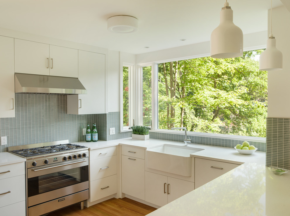 Example of a mid-sized trendy u-shaped light wood floor eat-in kitchen design in New York with a farmhouse sink, flat-panel cabinets, white cabinets, quartz countertops, blue backsplash, glass tile backsplash, stainless steel appliances and no island