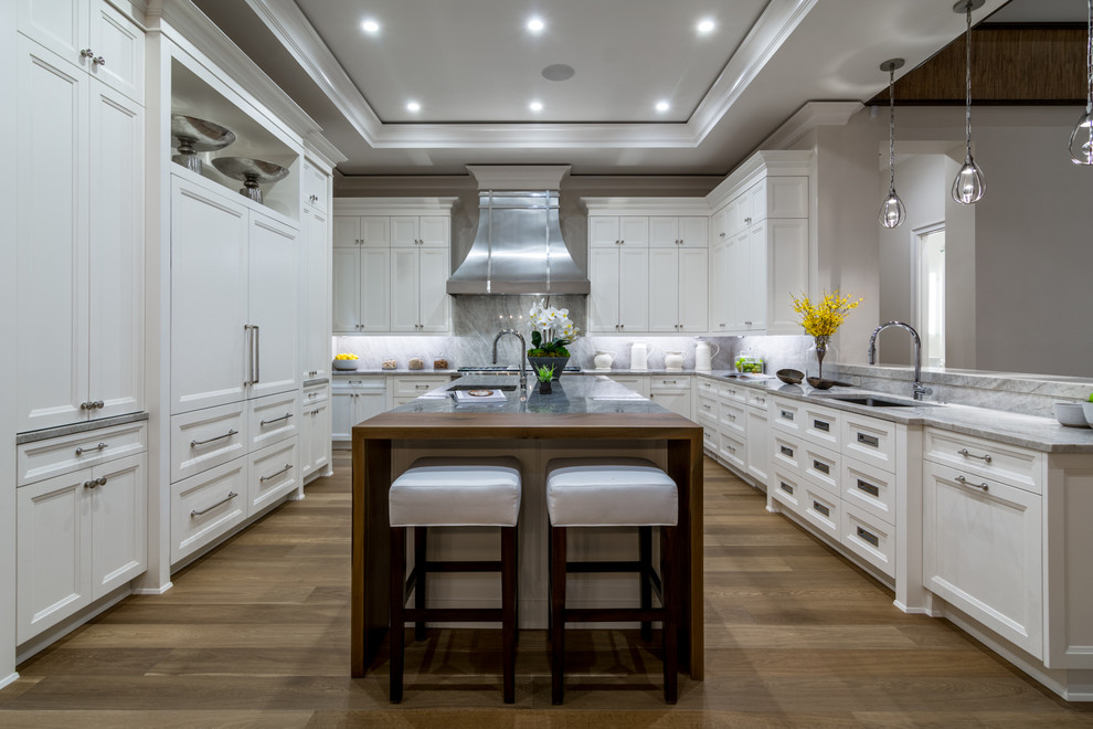 Inspiration for a large transitional u-shaped medium tone wood floor and brown floor kitchen remodel in Miami with an undermount sink, shaker cabinets, white cabinets, gray backsplash, paneled appliances and an island