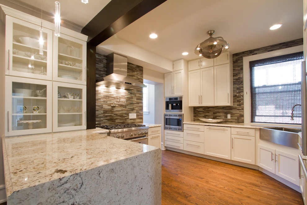 Mid-sized trendy u-shaped medium tone wood floor and brown floor enclosed kitchen photo in Denver with a farmhouse sink, shaker cabinets, white cabinets, granite countertops, metallic backsplash, glass tile backsplash, stainless steel appliances and a peninsula