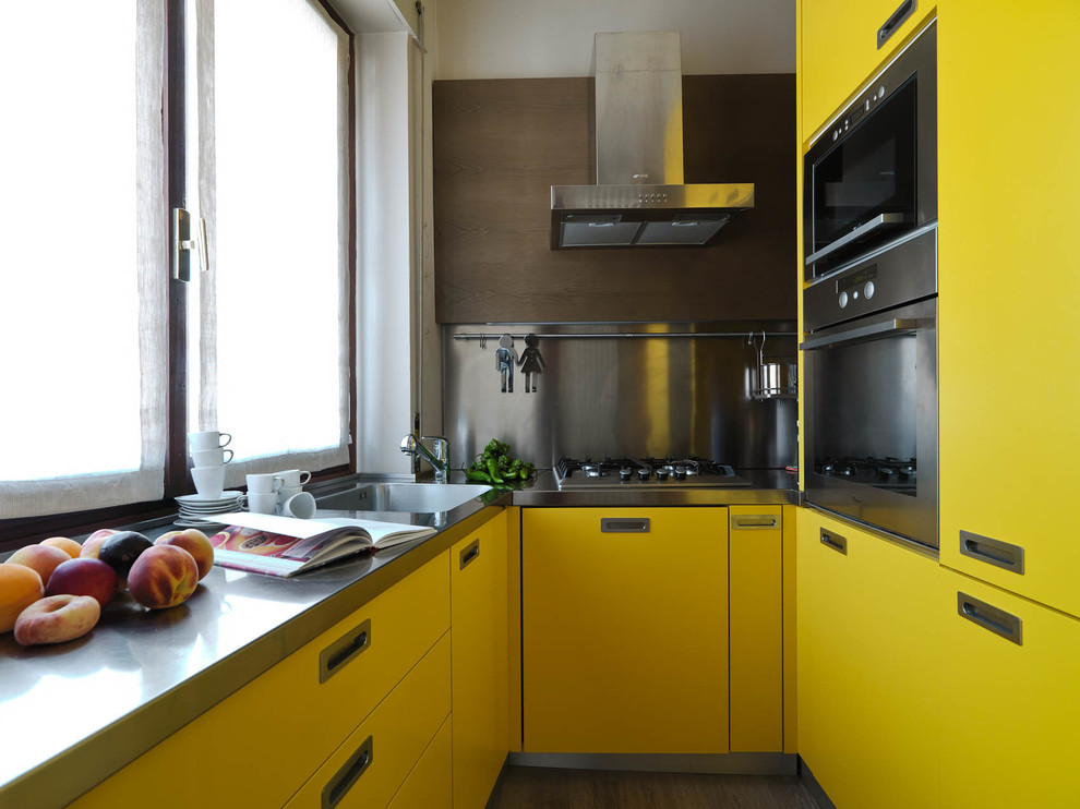 Пример оригинального дизайна: п-образная кухня в современном стиле с монолитной мойкой, плоскими фасадами, желтыми фасадами, столешницей из нержавеющей стали, фартуком цвета металлик, фартуком из металлической плитки и техникой из нержавеющей стали