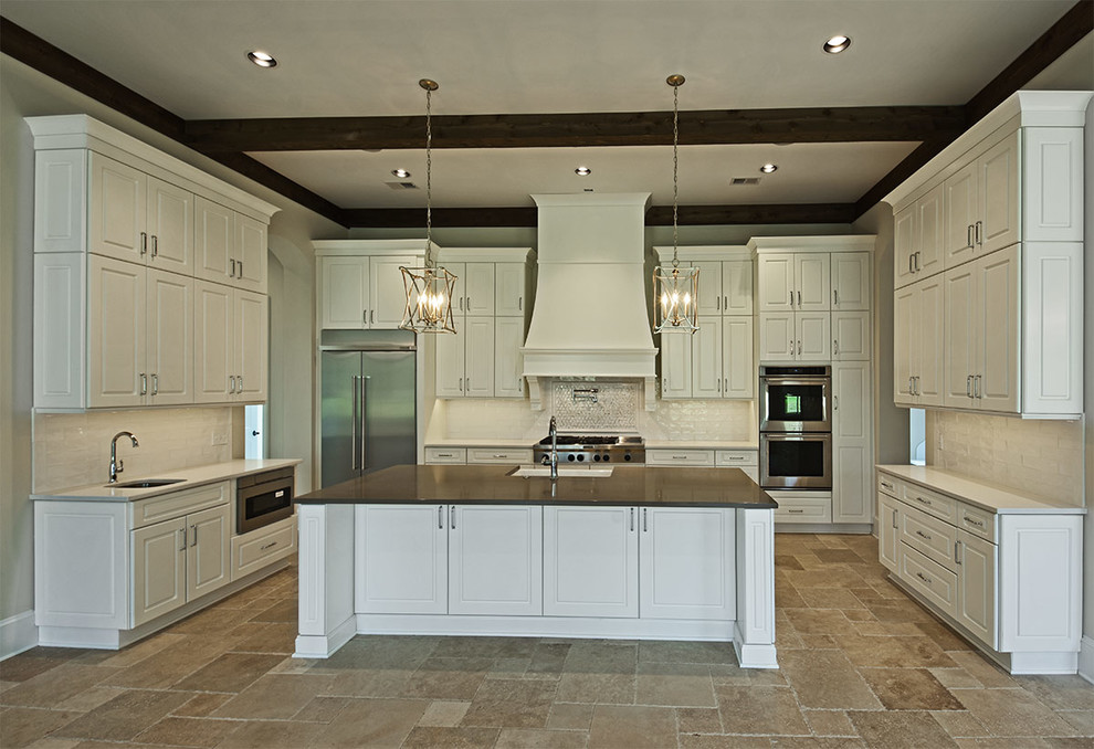 Design ideas for a medium sized traditional u-shaped open plan kitchen in Other with a belfast sink, raised-panel cabinets, white cabinets, composite countertops, white splashback, metro tiled splashback, stainless steel appliances, limestone flooring, an island and beige floors.