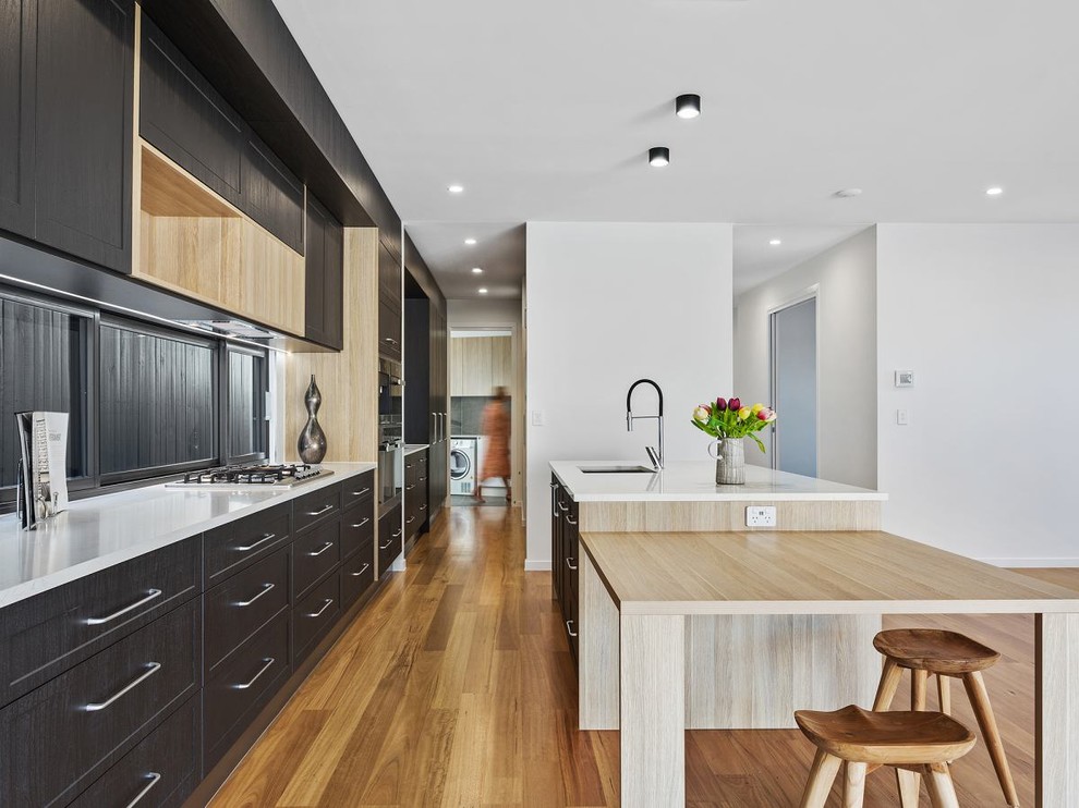 Example of a large trendy eat-in kitchen design in Brisbane with dark wood cabinets, solid surface countertops, window backsplash, stainless steel appliances and an island