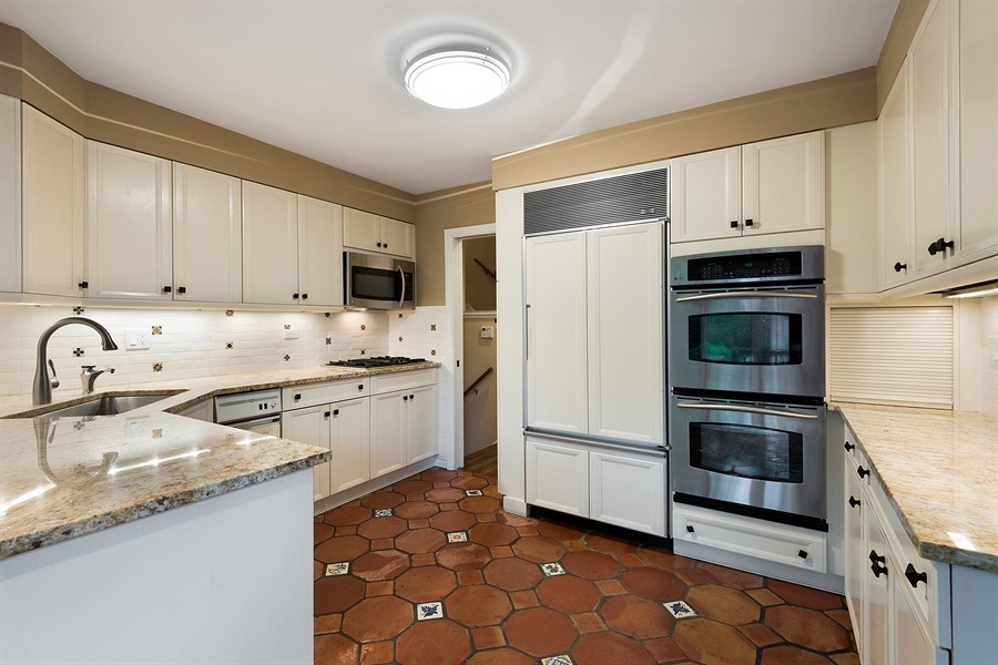 На фото: кухня в стиле ретро с белыми фасадами, фартуком из керамической плитки, техникой из нержавеющей стали и полом из терракотовой плитки