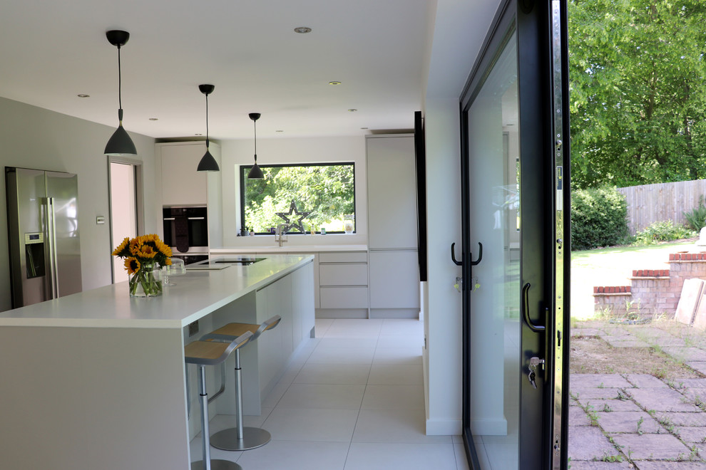 Photo of a large contemporary single-wall kitchen/diner in Hertfordshire with a built-in sink, flat-panel cabinets, grey cabinets, composite countertops, white splashback, ceramic flooring, an island, grey floors and white worktops.