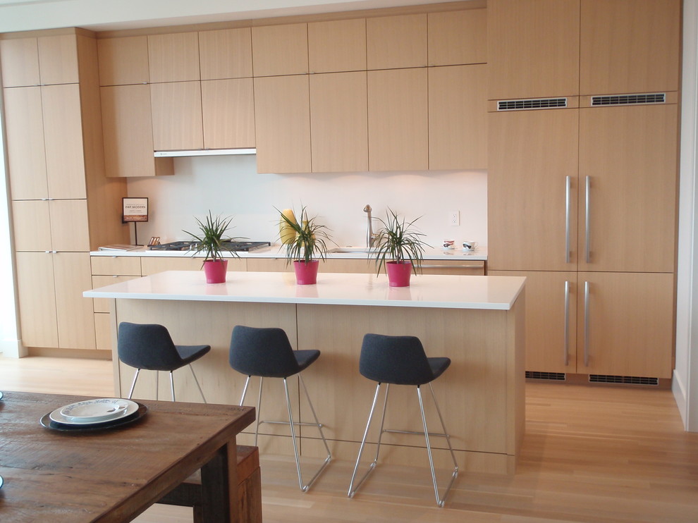 Diseño de cocina moderna con fregadero bajoencimera, puertas de armario de madera clara, salpicadero blanco, electrodomésticos con paneles, suelo de madera clara y una isla