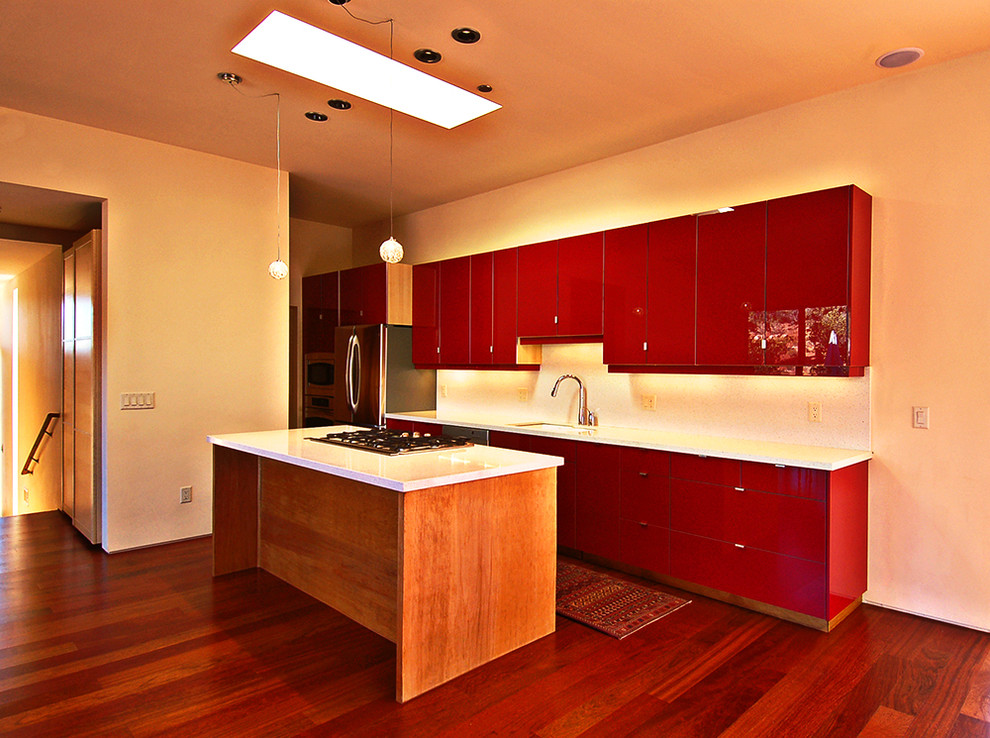 Foto på ett stort funkis linjärt kök med öppen planlösning, med en undermonterad diskho, släta luckor, röda skåp, bänkskiva i kvarts, vitt stänkskydd, rostfria vitvaror, mörkt trägolv och en köksö