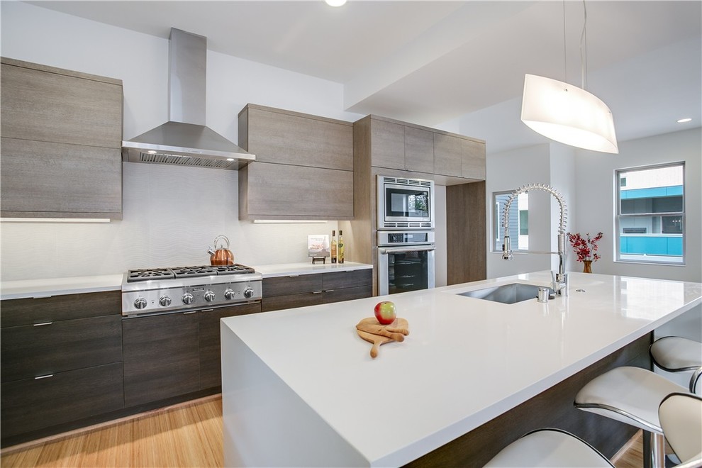 Imagen de cocinas en L minimalista abierta con electrodomésticos de acero inoxidable, una isla y armarios con paneles lisos