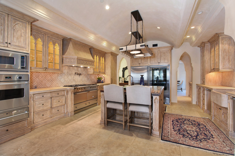 Geschlossene Mediterrane Küche in U-Form mit Landhausspüle, Glasfronten, hellen Holzschränken, Küchenrückwand in Beige, Küchengeräten aus Edelstahl und Kücheninsel in Orange County