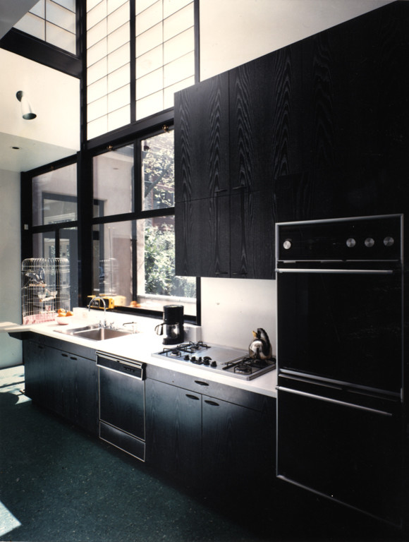 Стильный дизайн: большая прямая кухня-гостиная в стиле модернизм с накладной мойкой, плоскими фасадами, черными фасадами, столешницей из акрилового камня, черной техникой, бетонным полом, островом, черным полом и белой столешницей - последний тренд