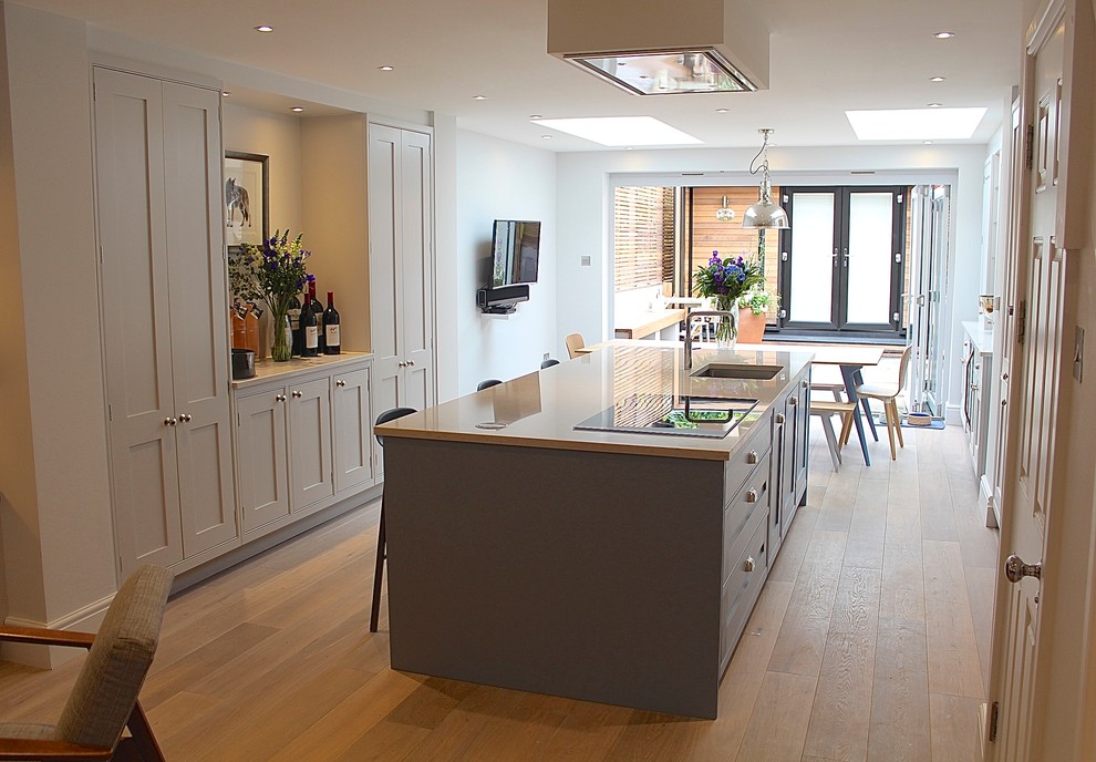 Medium sized classic open plan kitchen in London with a built-in sink, shaker cabinets, white cabinets, quartz worktops, stainless steel appliances, light hardwood flooring and an island.