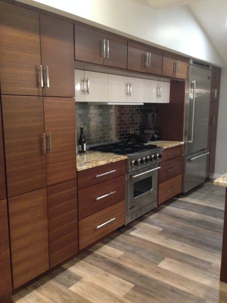 This is an example of a small contemporary galley kitchen/diner in Bridgeport with a submerged sink, flat-panel cabinets, medium wood cabinets, granite worktops, grey splashback, metal splashback, stainless steel appliances, vinyl flooring and an island.