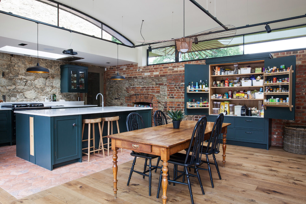 Design ideas for an expansive country u-shaped kitchen/diner in Kent with a built-in sink, recessed-panel cabinets, green cabinets, granite worktops, black appliances, terracotta flooring, an island, multi-coloured floors and white worktops.
