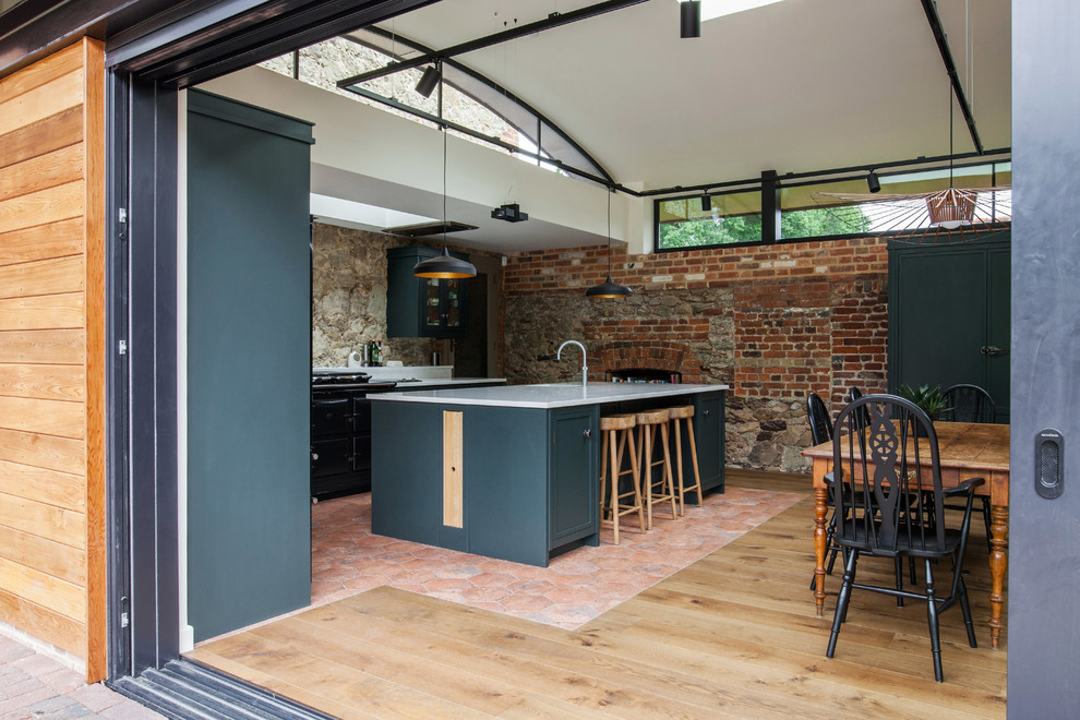 Expansive farmhouse u-shaped kitchen/diner in Kent with a built-in sink, recessed-panel cabinets, green cabinets, granite worktops, black appliances, terracotta flooring, an island, multi-coloured floors and white worktops.