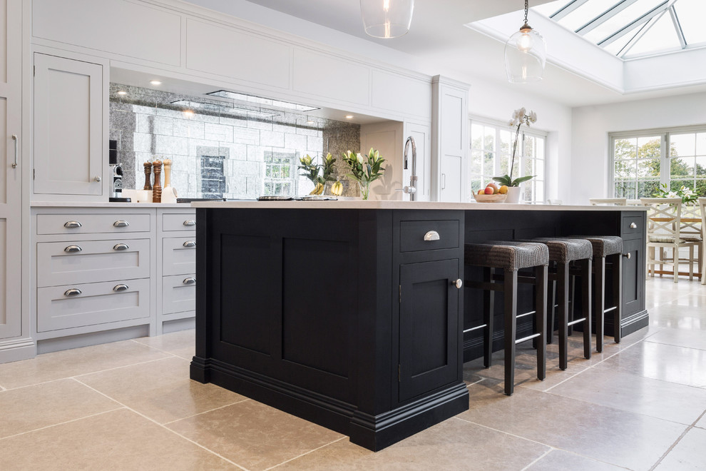Example of a large classic galley limestone floor and beige floor open concept kitchen design in Kent with an integrated sink, shaker cabinets, gray cabinets, quartzite countertops, metallic backsplash, mirror backsplash, black appliances, an island and white countertops