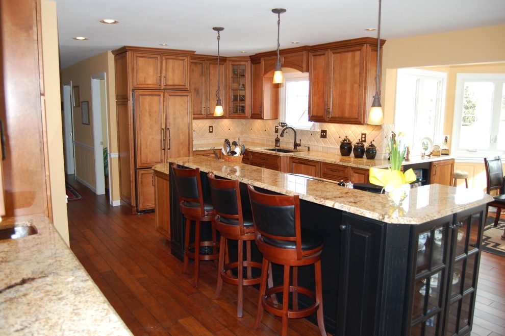 Example of a mid-sized classic l-shaped dark wood floor and brown floor enclosed kitchen design in Philadelphia with an undermount sink, raised-panel cabinets, brown cabinets, granite countertops, beige backsplash, ceramic backsplash, paneled appliances and an island