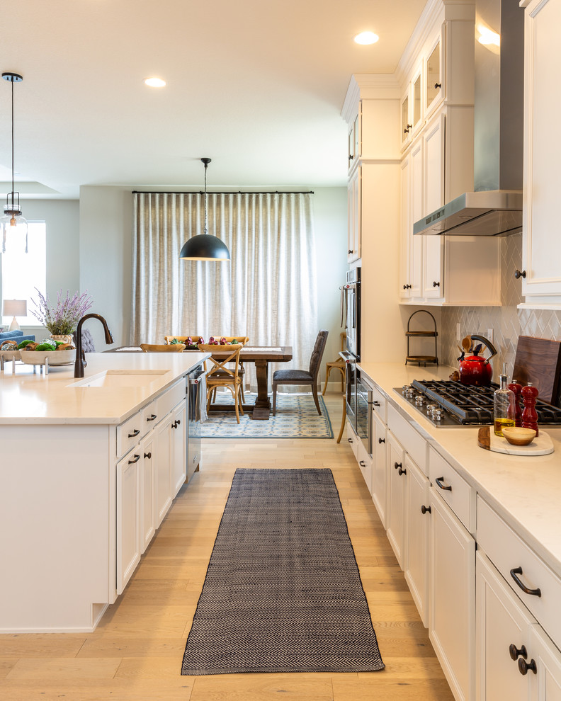 Inspiration for a mid-sized country light wood floor eat-in kitchen remodel in Denver with a farmhouse sink, recessed-panel cabinets, white cabinets, quartzite countertops, gray backsplash, ceramic backsplash, stainless steel appliances, an island and white countertops