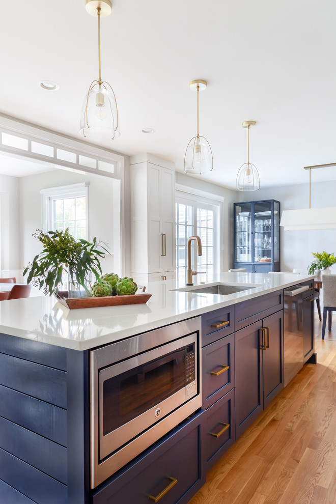 Example of a mid-sized transitional galley light wood floor and white floor eat-in kitchen design in Chicago with an undermount sink, shaker cabinets, quartz countertops, white backsplash, stone tile backsplash, stainless steel appliances, an island, white countertops and blue cabinets