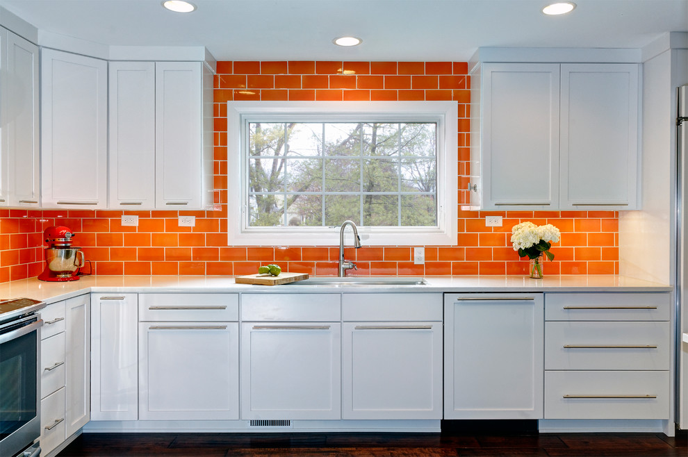 Inspiration for a contemporary l-shaped kitchen/diner in Columbus with a submerged sink, flat-panel cabinets, white cabinets, engineered stone countertops, orange splashback, ceramic splashback, stainless steel appliances, dark hardwood flooring and a breakfast bar.