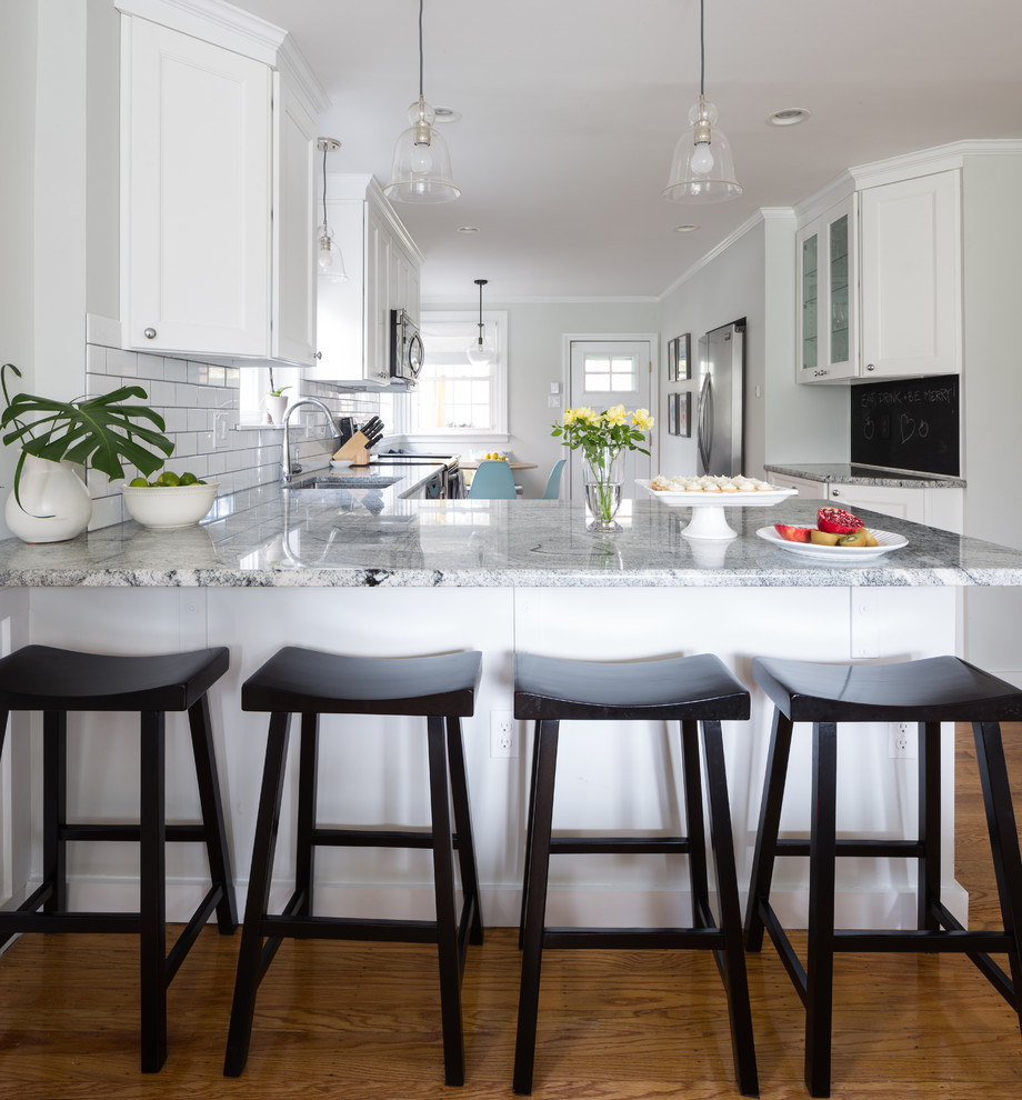 Example of a mid-sized eclectic l-shaped medium tone wood floor eat-in kitchen design in Philadelphia with an undermount sink, shaker cabinets, white cabinets, granite countertops, white backsplash, ceramic backsplash, stainless steel appliances and a peninsula